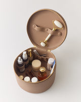 Round cosmetic case with skincare products and face roller inside.