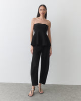 Person wearing a strapless top and pants with open-toe footwear stands in a room.