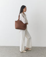 Person holding a large handbag, wearing a long-sleeve top and wide-leg pants.