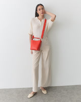Person standing with a red crossbody bag, wearing a collared shirt and pants.