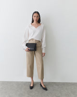 Person in blouse and pants holding a small bag, standing against a plain background.