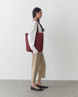 Person standing sideways holding a large tote bag, wearing a sweater and pants.