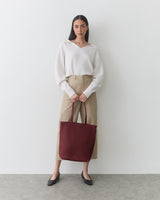 Person holding a large tote bag, standing against a plain background.