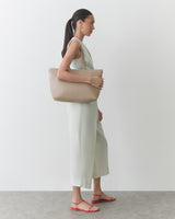 Person wearing a sleeveless dress and sandals, carrying a tote bag over one shoulder.