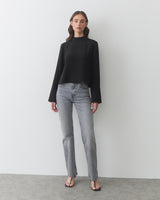 Person in long-sleeve top and jeans, standing on a plain floor.