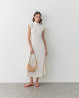 Woman in long sleeveless dress holding a handbag, wearing sandals.