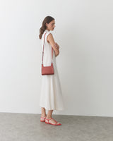 Person in sleeveless dress with crossbody bag and sandals standing against a plain backdrop.