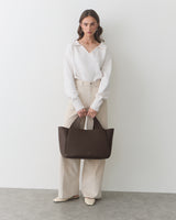 Person holding a large handbag wearing long-sleeve top and wide-leg pants.