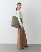 Person with tote bag, wearing long-sleeve top and wide-leg pants, standing sideways.