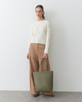 Person standing with a tote bag, wearing a long-sleeve top and wide-leg pants.