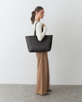 Person standing with large tote bag, wearing long-sleeve top and wide-leg pants.