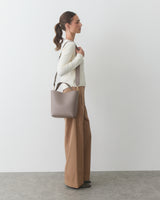 Person standing with a shoulder bag, wearing a long-sleeve top and wide-leg pants.