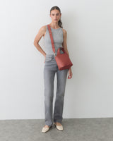 Person standing, wearing sleeveless top, jeans, holding red bag with shoulder strap.