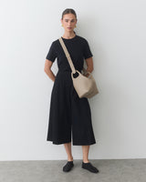 Person in black outfit with crossbody bag stands indoors.