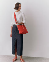 Person wearing a long skirt and top, holding a bag and standing in a neutral space.