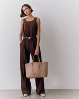 Person in sleeveless top and trousers holding a large tote bag.