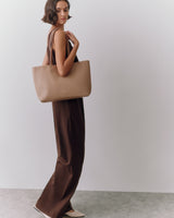 Person in a dress holding a large tote bag standing sideways.