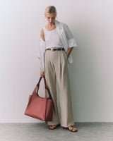 Person in a white top and slacks holds a large handbag and wears sandals.