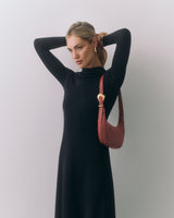 Woman in a long dress with a shoulder bag adjusting her hair