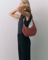 Person wearing a sleeveless top and pants, holding a handbag on shoulder.