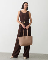 Person wearing a sleeveless top and pants, holding a tote bag.