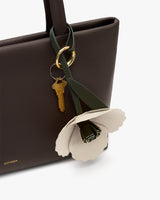 Handbag with a flower keychain and two gold keys attached.