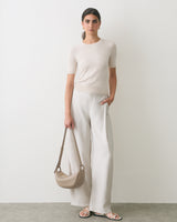 Person wearing short-sleeve top and wide-leg pants holds a shoulder bag and wears sandals.