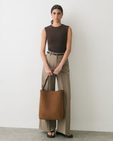 Person standing with tote bag, wearing sleeveless top, pants, and sandals.