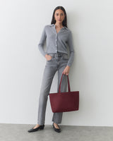 Person standing with a handbag wearing a button-up shirt and jeans.