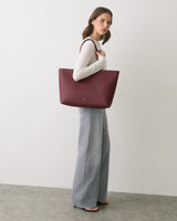 Person carrying a large tote bag over shoulder, wearing long-sleeve top and wide-leg pants.