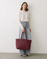 Person standing with a large handbag wearing a long-sleeve shirt and jeans.