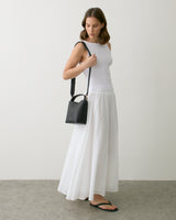 Person in sleeveless top and long skirt holding a small shoulder bag.