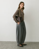 Person wearing buttoned cardigan, wide pants, flats, and holding a chain-strap bag.