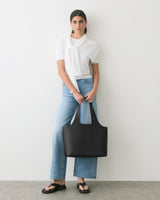 Person standing with a large handbag, wearing jeans and sandals, sweater draped over shoulders.
