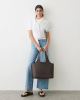 Person standing, wearing a tied shirt and jeans, holding a handbag with open-toed sandals.