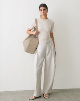 Person standing with a travel bag wearing short-sleeve shirt and wide-leg pants.