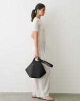 Person standing with a geometric handbag wearing a short sleeve top and loose pants.