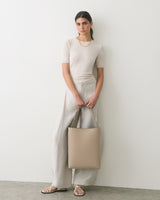 Person standing with a tote bag wearing a casual outfit and sandals.