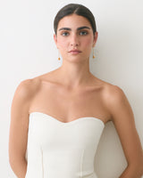 Person wearing a strapless top with drop earrings standing against a plain background.