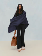 Woman standing with a draped garment and holding a bag.