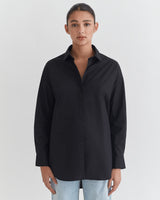 Woman in a button-up shirt and jeans standing against a white background.