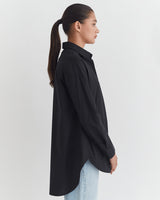 Woman in a buttoned shirt and jeans viewed from the side with hair in a ponytail.