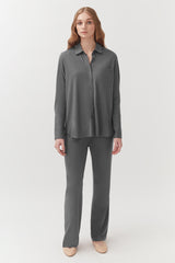 Woman standing in a buttoned shirt and pants with a neutral background.