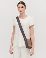 Woman standing with a crossbody bag, looking at the camera.