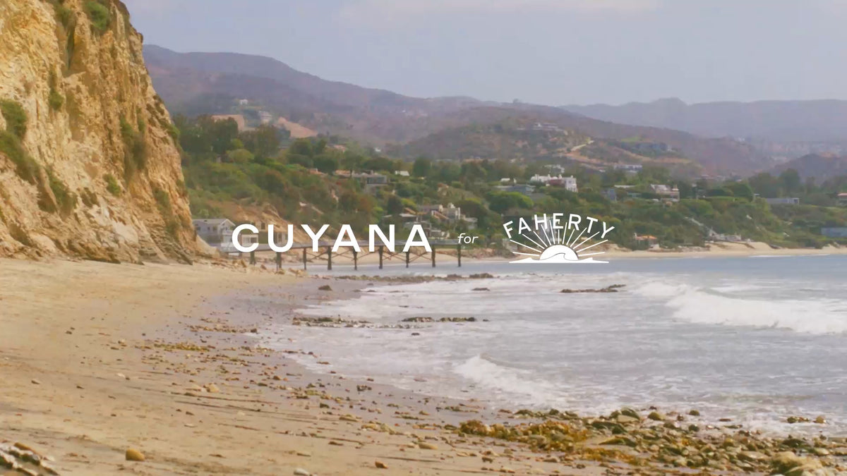 Beach shoreline with cliffs and distant hills in background. Text overlay says Cuyana for Faherty.