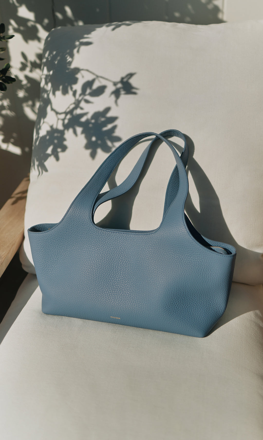 Handbag sitting on a cushioned chair with plant shadows in background.
