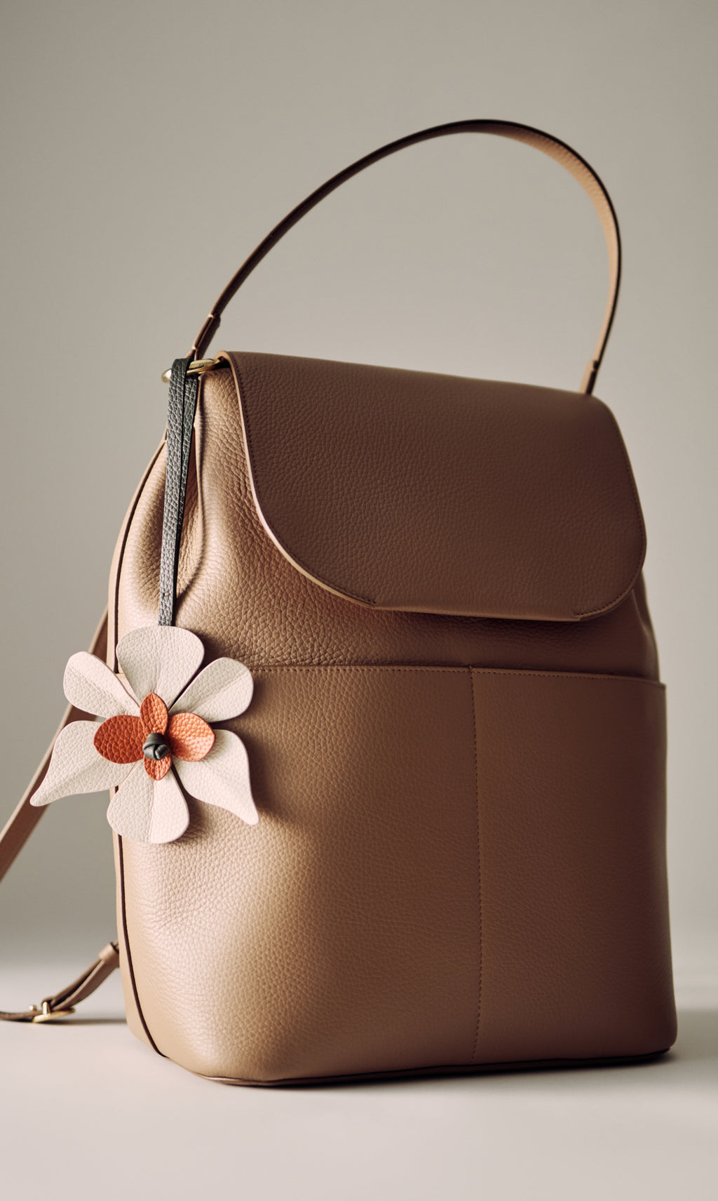 Backpack with flower charm and handle displayed on surface.