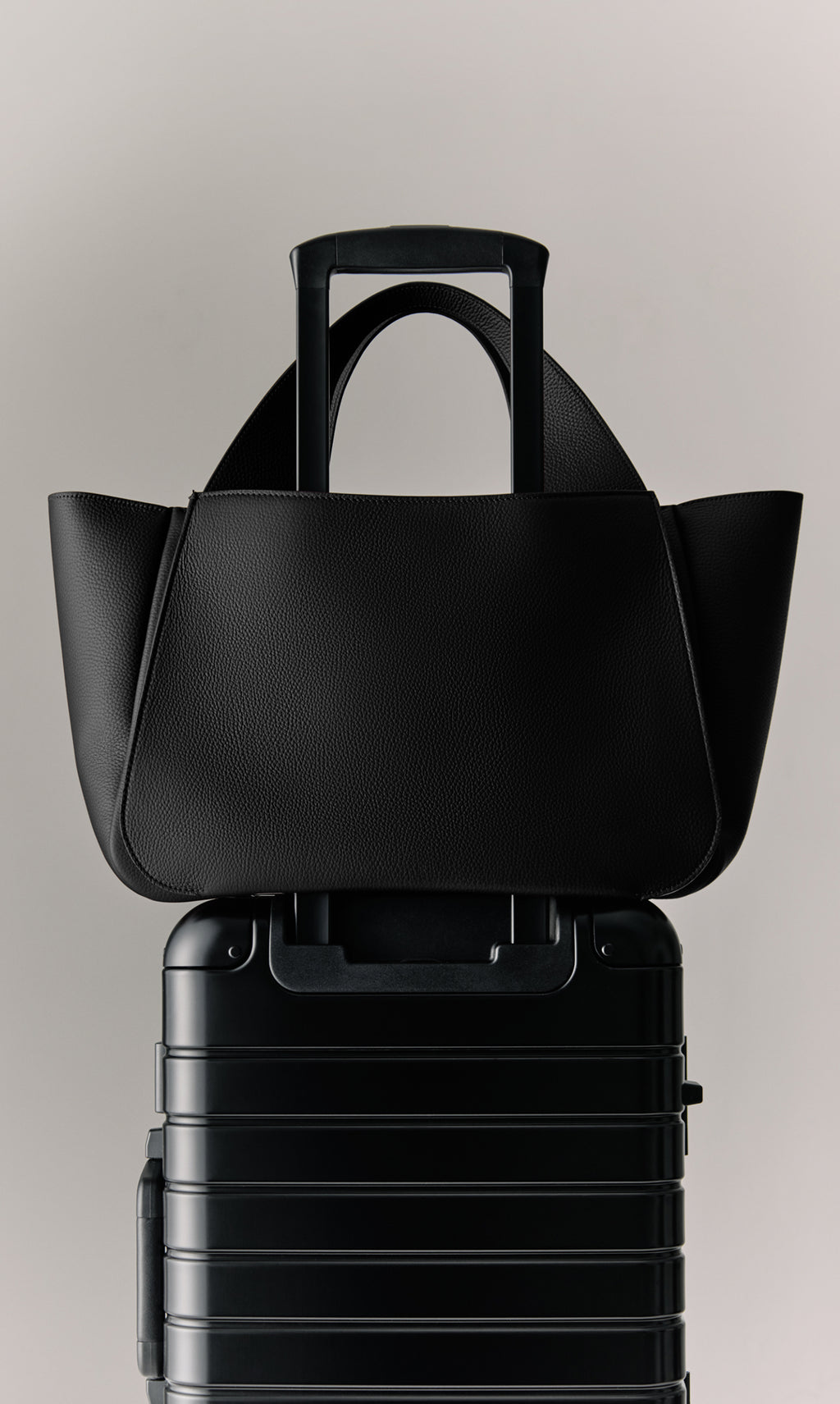 Bag on top of a wheeled suitcase with extended handle.