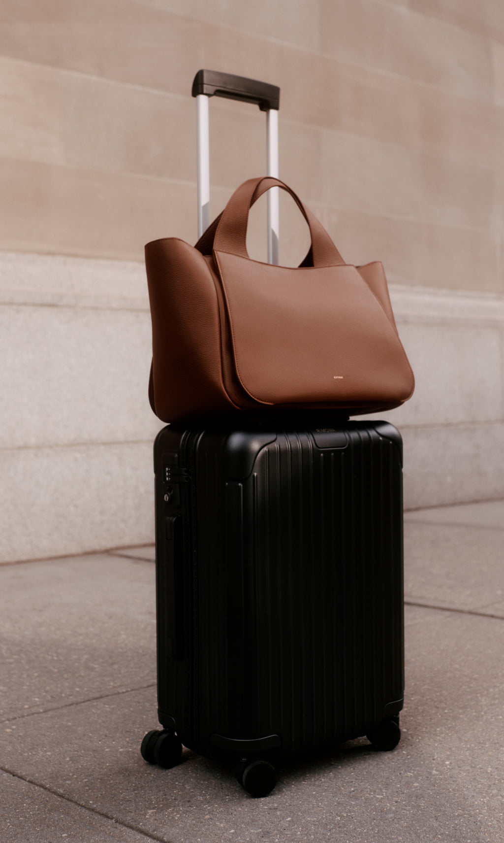 Rolling suitcase with a handbag on top near a wall.