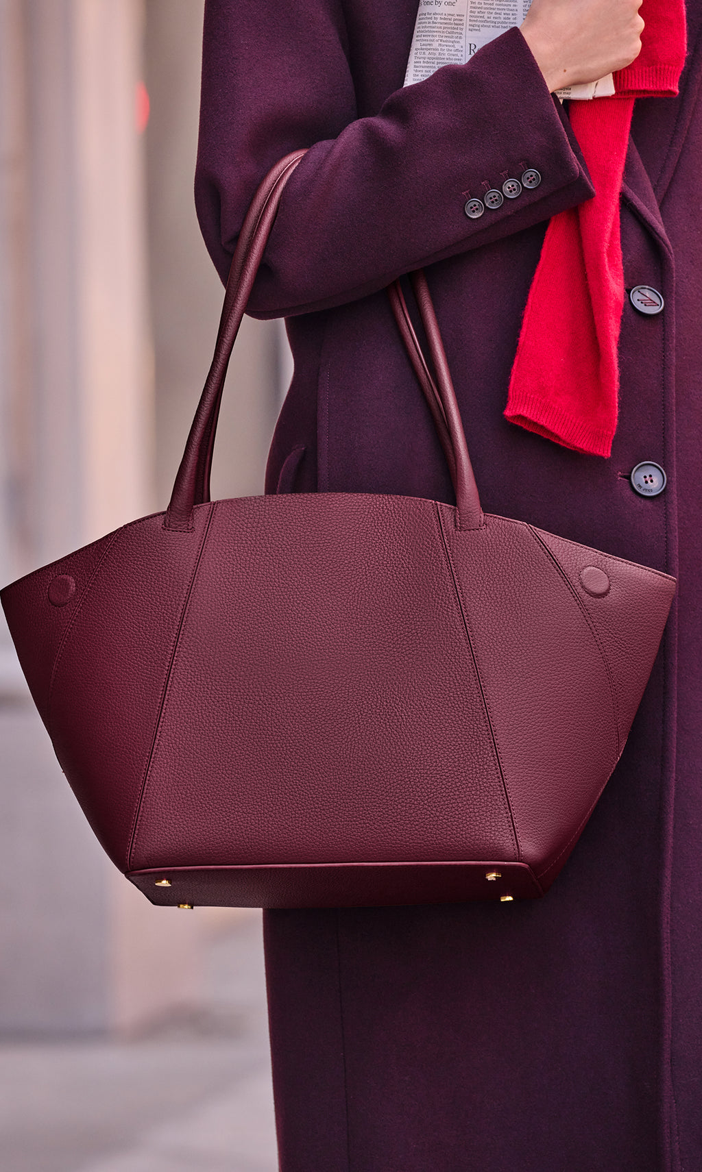 Person holding a large handbag and a scarf, wearing a long coat.